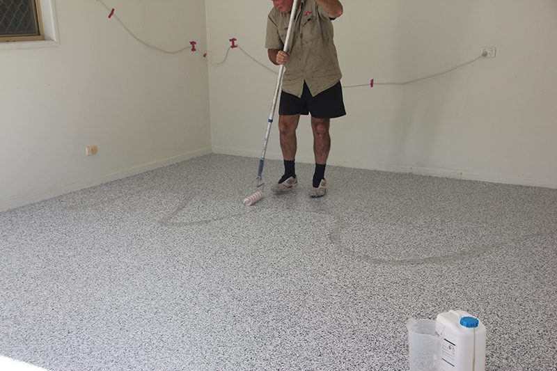 An installer rolling out a clear Ezypoly topcoat on top of Resin Vinyl flake in a residential garage.