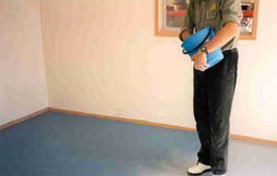 An installer broadcasting a blue non-slip particle out of a bucket onto the epoxy basecoat.