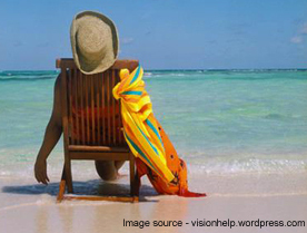 A person enjoying their holiday sitting on the beach in a deck chair.
