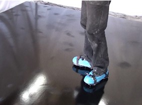 An installer standing on top of a glossy black basecoat that has just been sanded in some areas to smooth out small lumps and clumps.