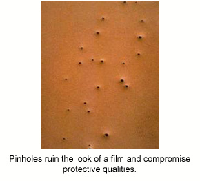 A close-up photo of large, visible pinholes in a brown protective epoxy coating.