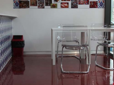 The red decorative epoxy floor with a table and some modern, clear chairs waiting for patrons to use.