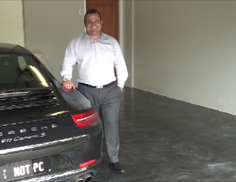 The smiling homeowner standing beside his black Porsche that's parked in the garage with the new metallic epoxy floor.