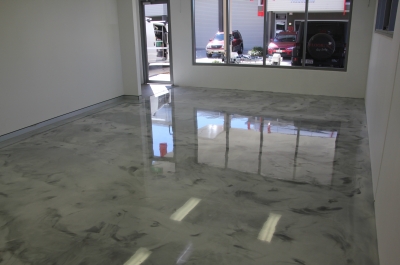 The glare from the front window of the small commercial office and warehouse showing the high-gloss finish of the metallic epoxy floor.