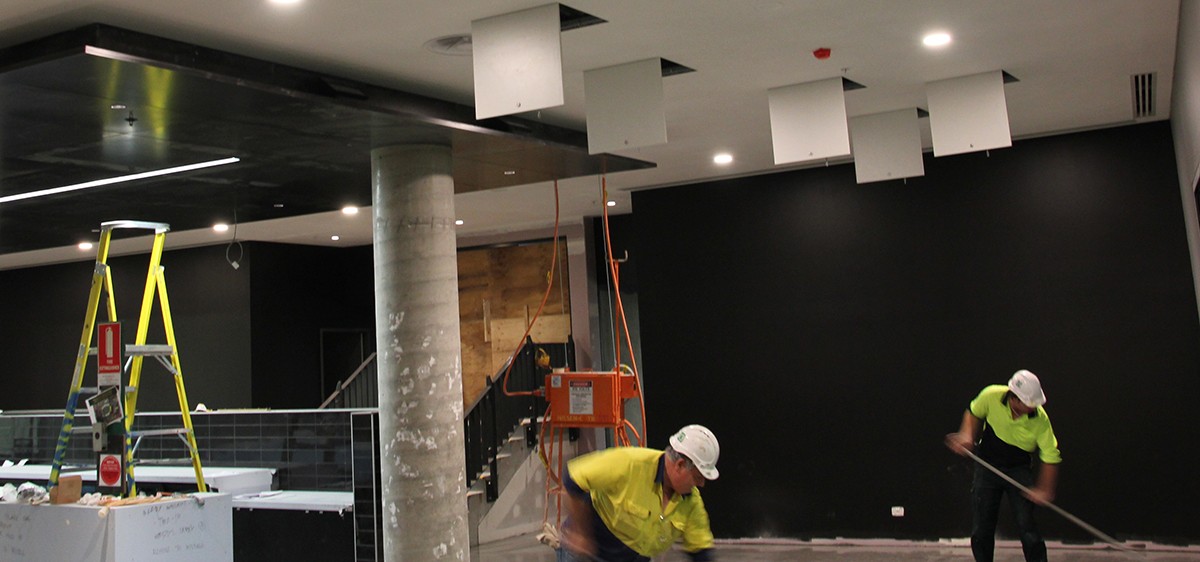 Resin flooring installers applying on a crowded work site with an electrician also doing work on the roof.