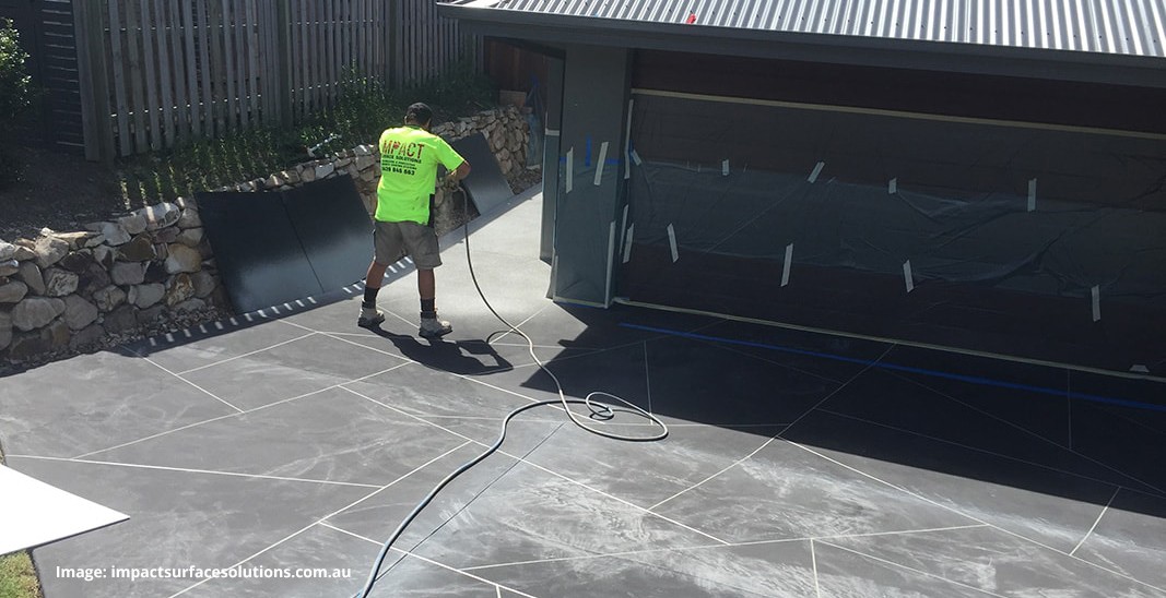 An installer using spraying equipment to apply a decorative concrete resurfacing product onto a driveway.
