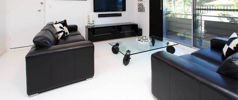 A pristine white epoxy floor and contrasting black furniture in the living room of a Brisbane City apartment.