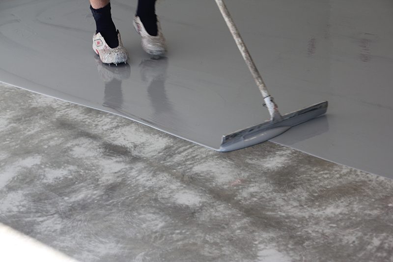 An epoxy rollcoat being applied with a squeegee directly to concrete without a primer underneath.
