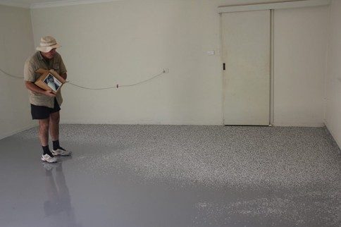 An epoxy flake flooring installer in spiked shoes broadcasting flake into a wet film.