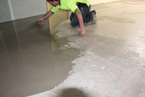 An installer on his knees trowelling down a levelling compound to make the floor flat before the epoxy flake floor is applied.