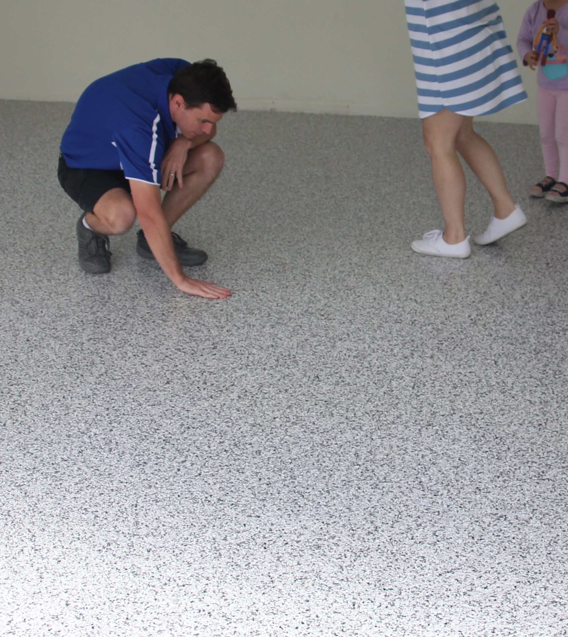 An epoxy flooring installer crouching down on an epoxy garage floor to run his hand across the finish.