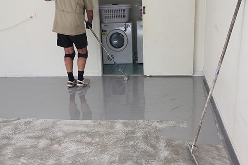 An installer applying a grey garage floor epoxy with a roller.