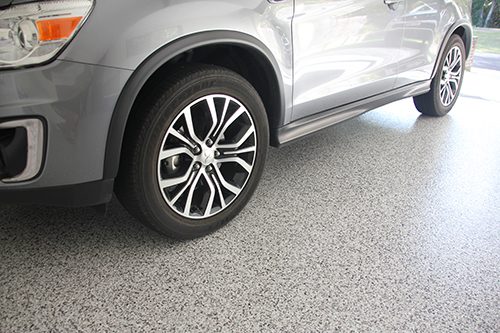 A close up of the passenger side of a car that's sitting on top of a new garage floor epoxy.