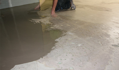 An installer on his knees trowelling down a levelling compound made from the Filler additive.