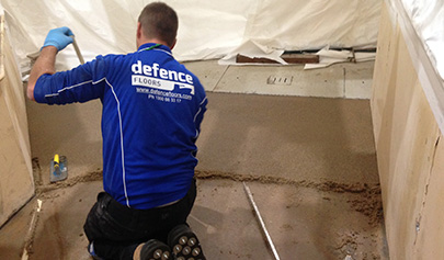 An installer on his knees trowelling down a screed to level an industrial floor.