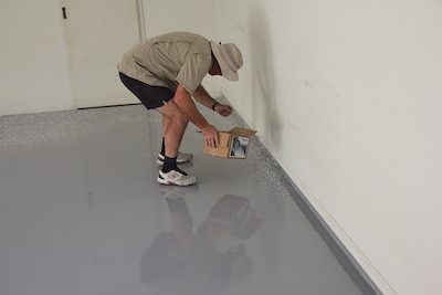 An installer broadcasting flakes onto an Ezypoxy Rollcoat basecoat in a residential garage.