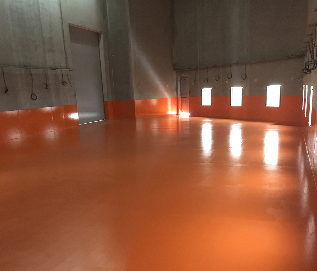 An empty factory warehouse after Jaxxon industrial coatings had been applied in a custom orange colour.