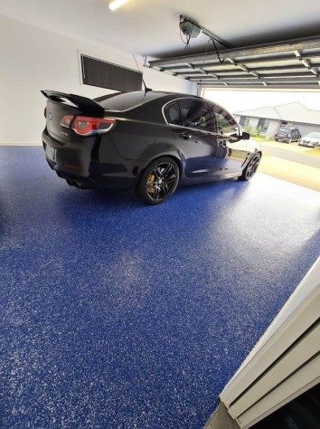 A new car sitting on top of a brilliant blue flake floor in a residential garage, which was completed with a clear topcoat of Ezypoly.