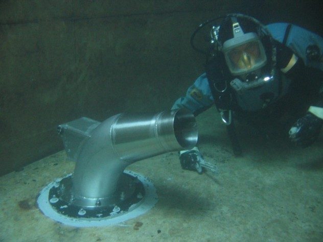 A diver looking at the camera as they apply Scubapoxy around the base of a nozzle installed in a tank.
