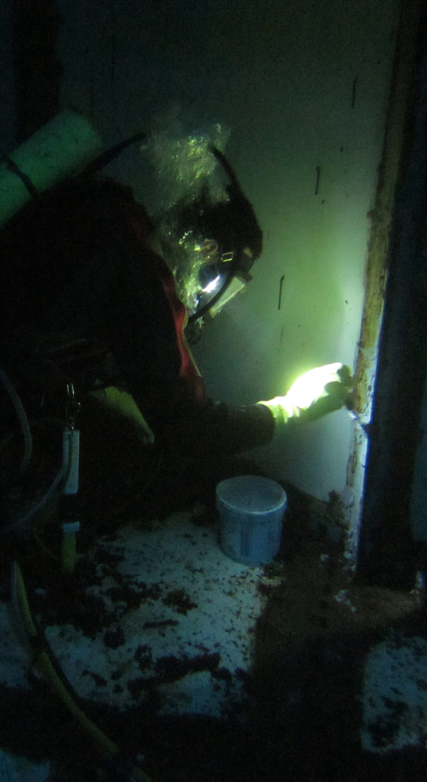 A diver brushing out Scubapoxy 1715 in a dark tank using the light on their helmet to see.