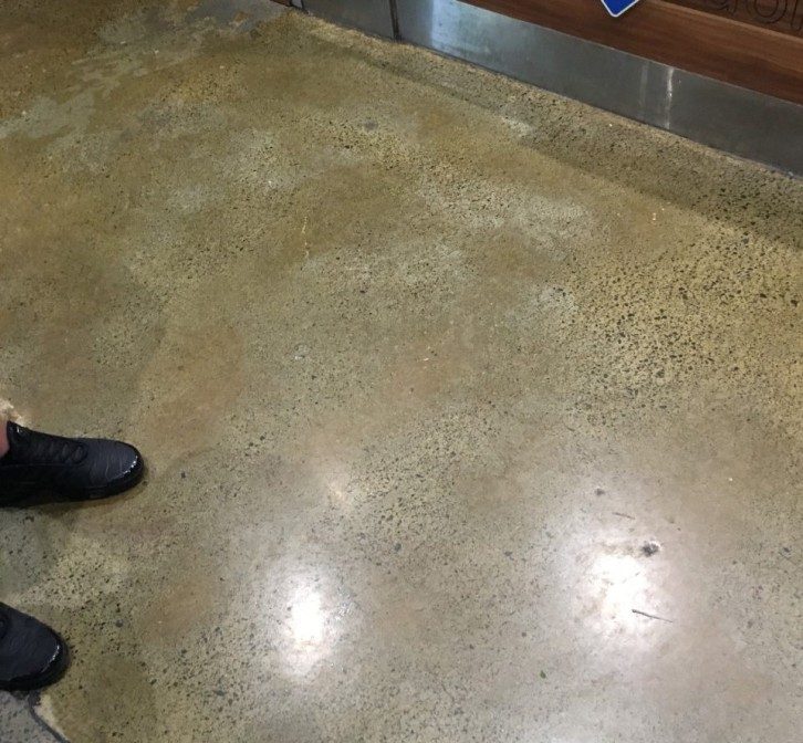 A person standing on a polished concrete floor with a patchy, uneven appearance.