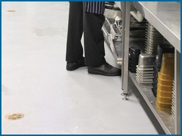 Close up of a chef standing on a commercial epoxy floor in a commercial kitchen.