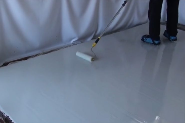 An installer rolling out a light grey basecoat for the non-slip epoxy floor.