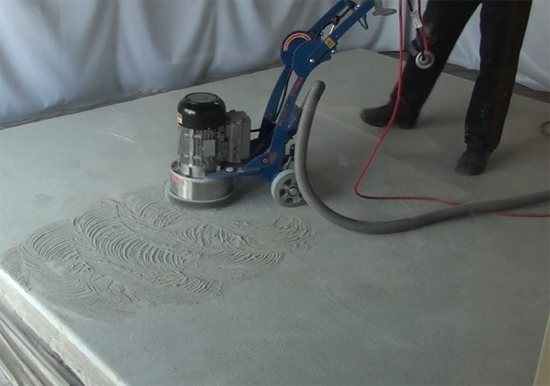 An installer uses a mechanical grinder to prepare the concrete for non-slip epoxy flooring on a training slab.