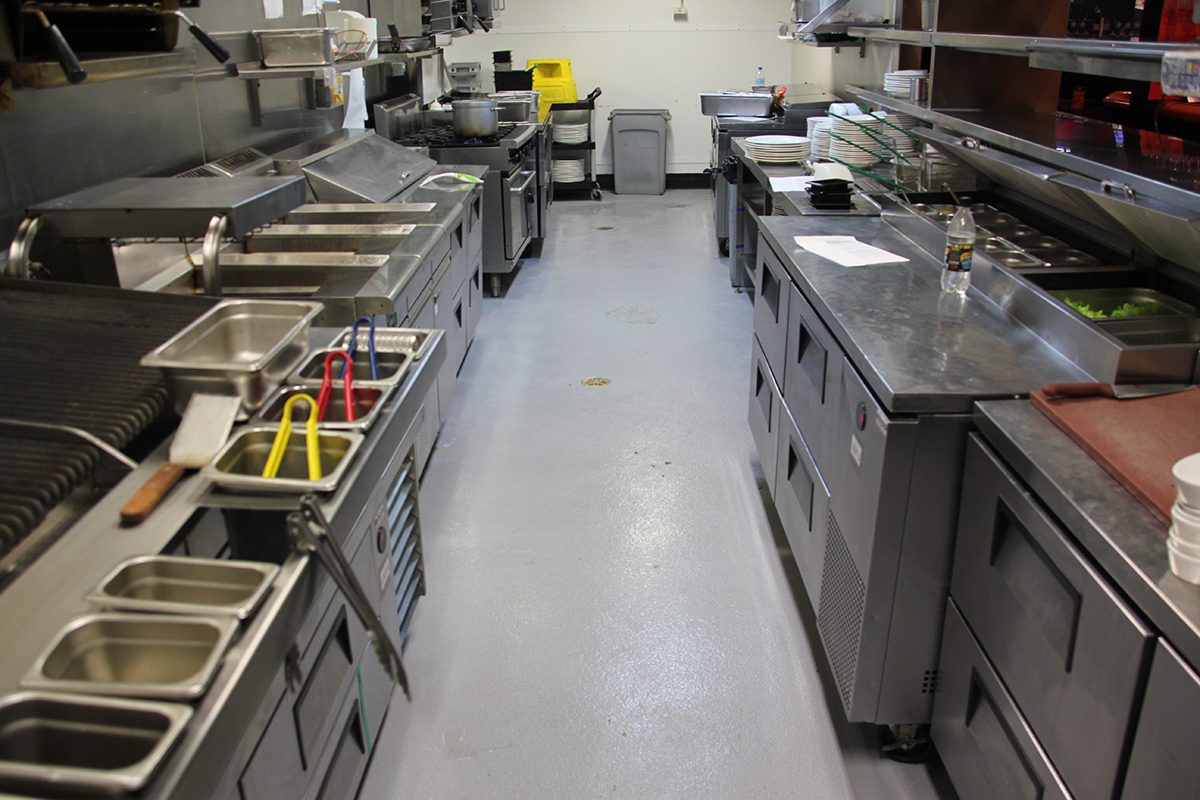 The corridor of the commercial kitchen showing the new non-slip epoxy floor flowing seamlessly among the cooking equipment.