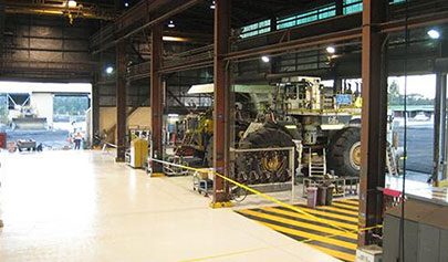 A large piece of mining machinery sitting on top of a Resin Grip system in a workshop with yellow and black line marking.