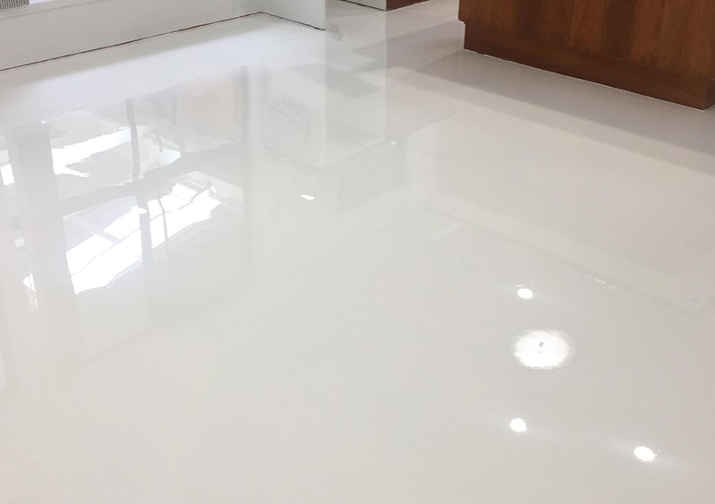 A close up of a high-gloss, white residential epoxy floor in a residential kitchen showing the reflection of lights and window.