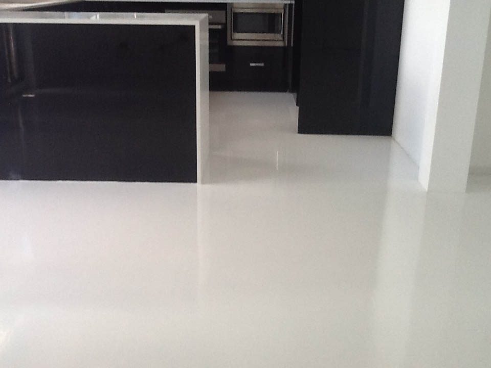 The pure white epoxy floor stretching across the living area and into the kitchen of the apartment.
