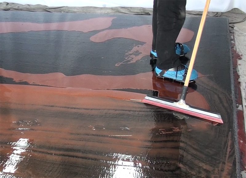 An installer using a squeegee to spread an epoxy topcoat with copper metallic pigments over a black basecoat.