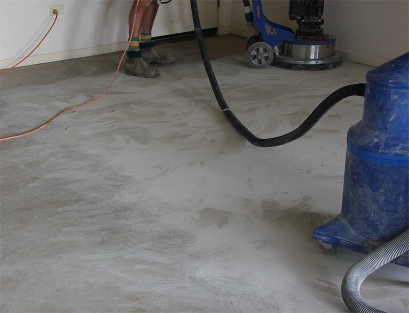 An installer uses a mechanical grinder to prepare concrete for metallic epoxy flooring in a garage.