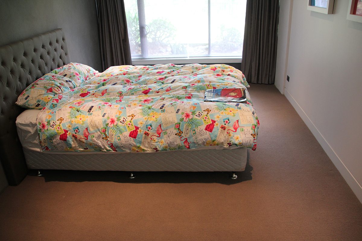 One of the downstairs bedrooms with a large double bed in the middle of the room sitting on the old, water-damaged carpet.