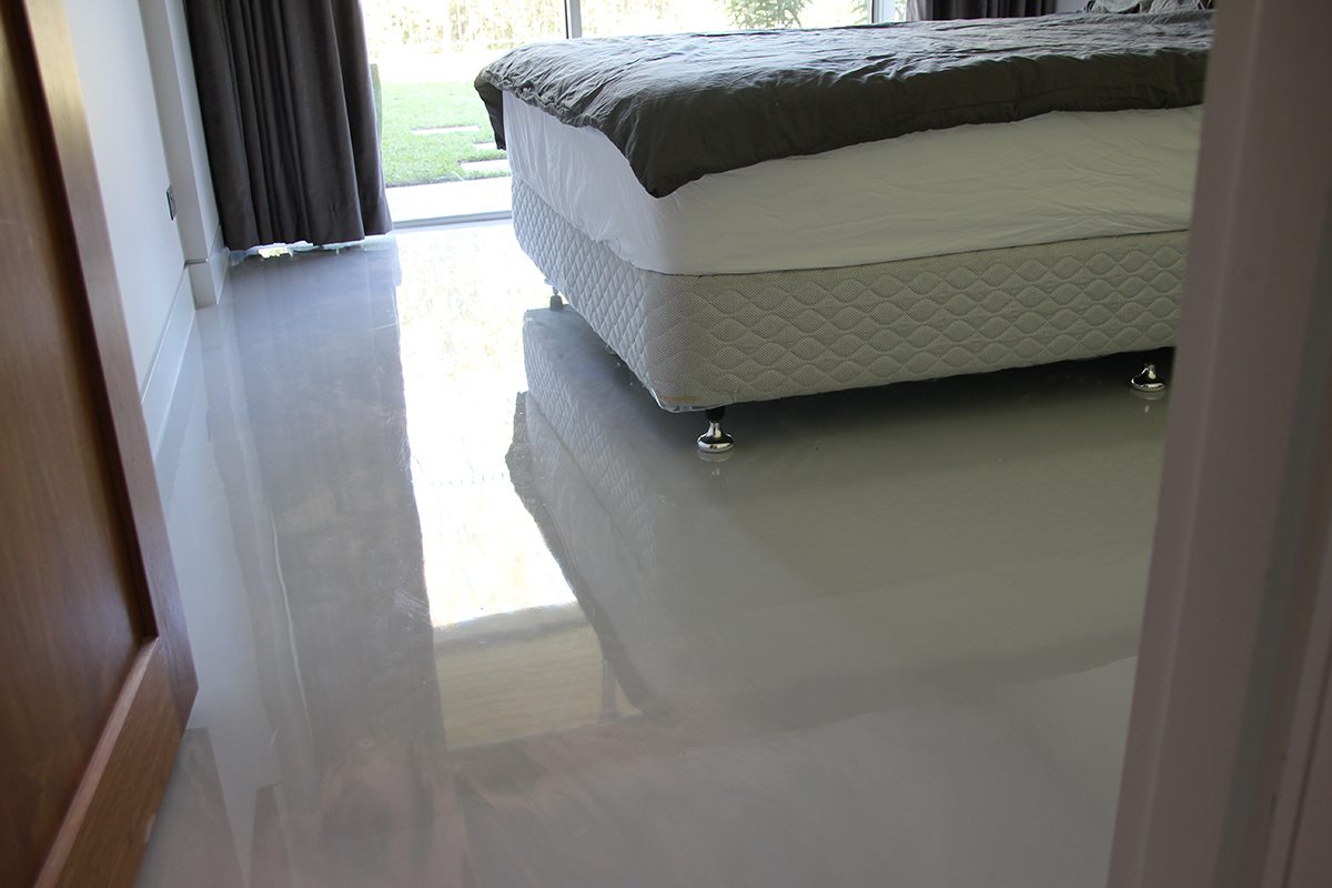 One of the downstairs bedrooms with a large double bed in the middle of the room sitting on the new, high-gloss metallic epoxy floor in a pearl colour.