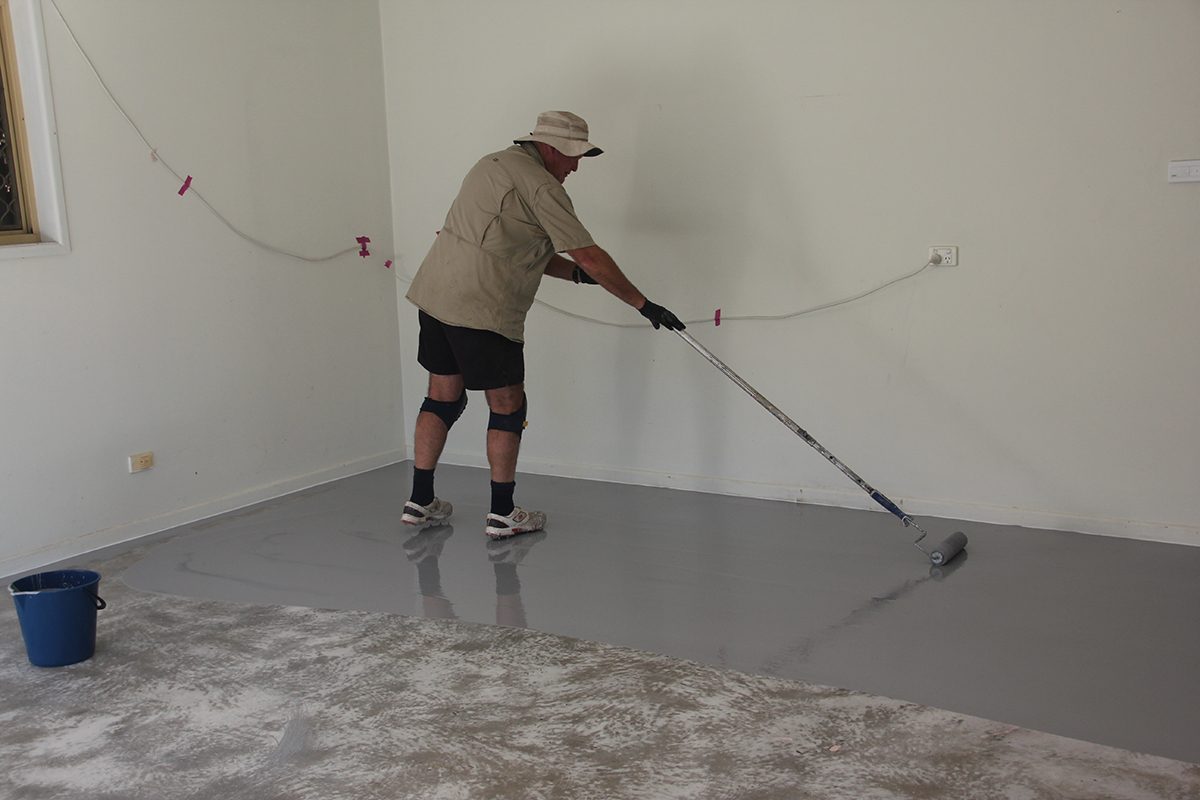 An installer rolling out a light grey basecoat for the garage epoxy flake floor.