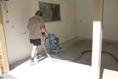 An installer uses a mechanical grinder to prepare the surface for epoxy flake flooring in a garage.